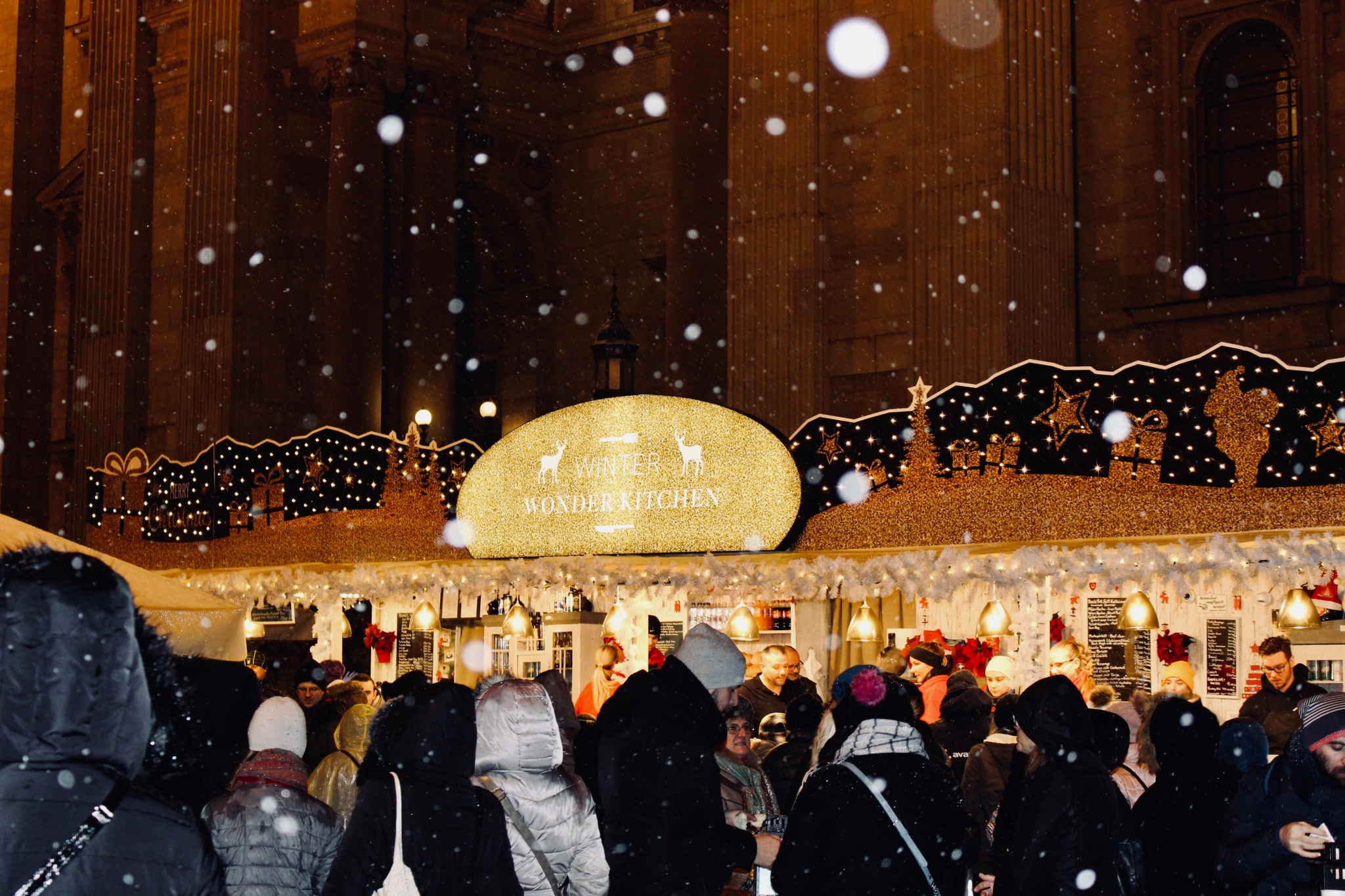 Ein gut besuchter Adventmarkt bei Nacht und Schneefall
