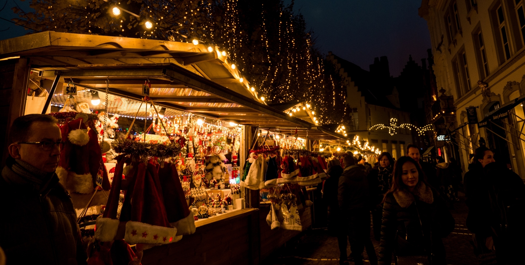 Blick auf einen festlich beleuchteten Weihnachtsmarkt mit Ständen und Besuchern