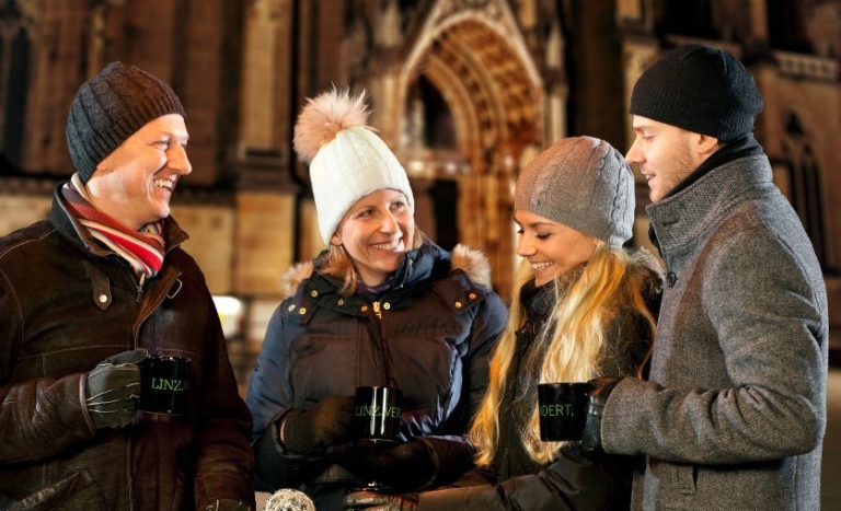Vier Menschen in guter Stimmung trinken Glückwein vor dem Dom