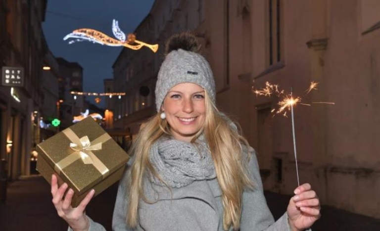 Frau mit Geschenk und Sternspritzer in weihnachtlich dekorierter Stadtstraße