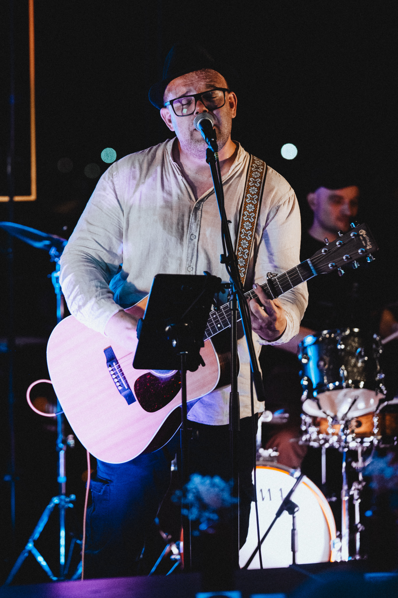 Coinflip Cutie performing live on stage. The singer plays acoustic guitar and sings into a microphone, with the drummer visible in the background.