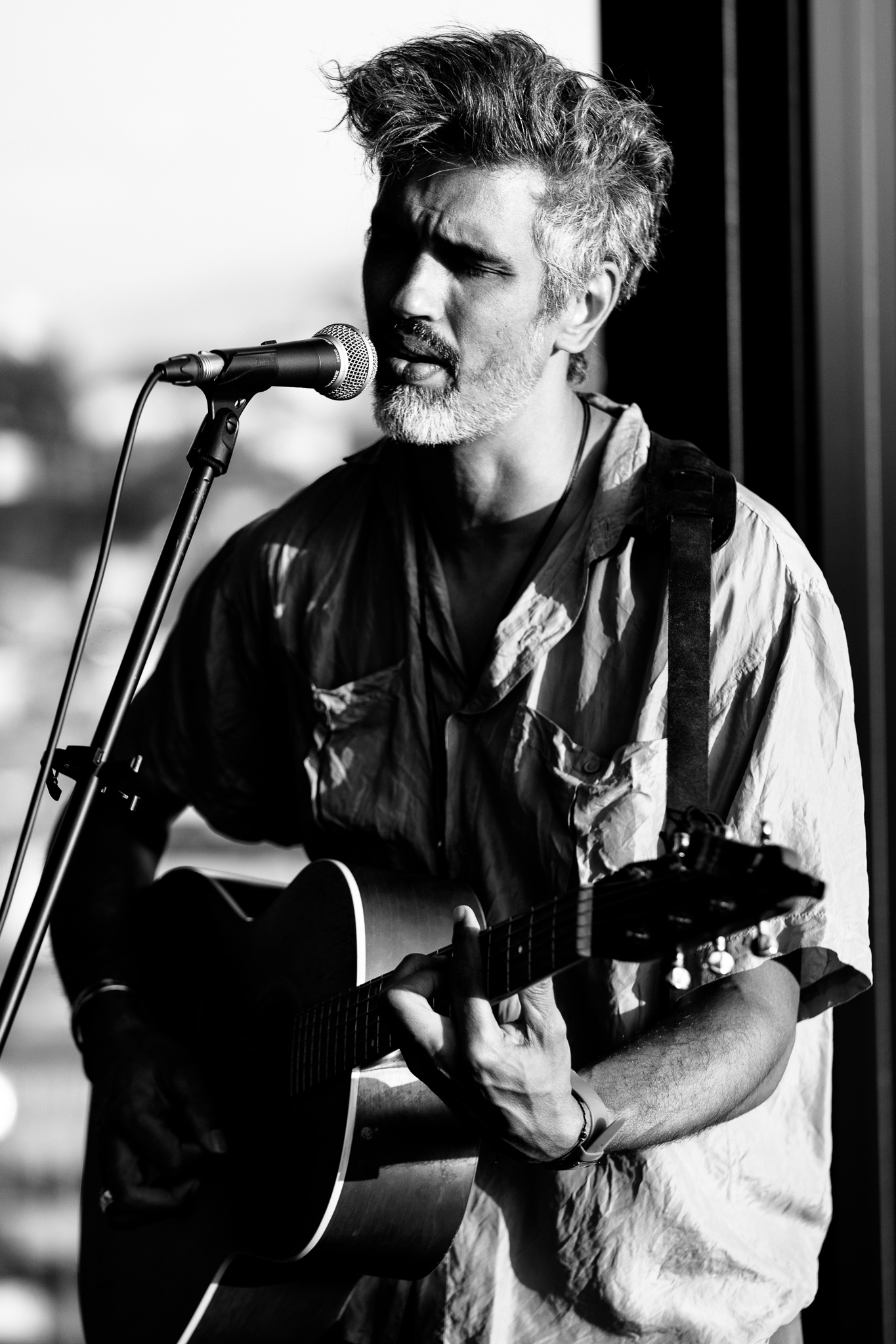 Schwarz-Weiß-Porträt von Phillip Bracken beim Singen und Gitarrespielen während eines Live-Konzerts in der hu:goes14 Rooftop Bar.