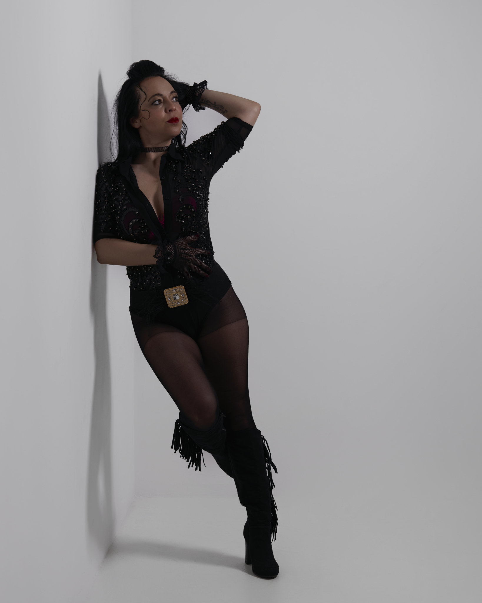 Jasmine Wallner posiert in schwarzem Bühnenoutfit vor einer hellen Wand und blickt ausdrucksstark zur Seite.