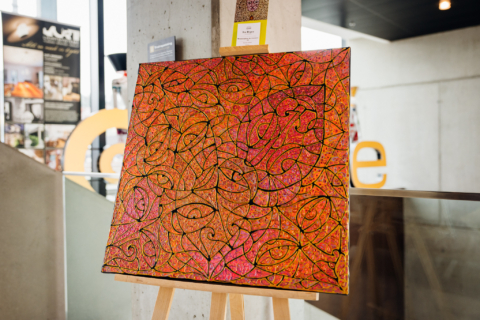 Large abstract artwork by Ira Repey in vibrant shades of orange, pink and red displayed on a wooden easel in the Trainspotting Lounge at arte Hotel Salzburg. The composition features numerous intertwined organic shapes and stylised eyes.
