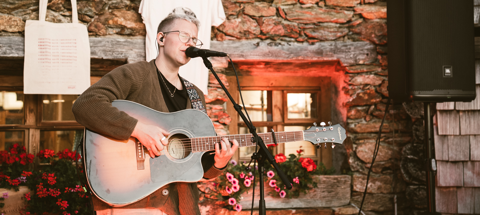 Souph singing into a microphone while playing an acoustic guitar during a live performance.